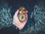 person holding round gold-colored compass